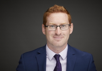 Red-headed man wearing glasses, a blue jacket, and a tie