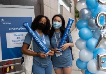 Two women in blue shirts next to blue and white balloons
