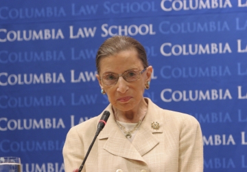 Ruth Bader Ginsburg standing at a podium in front of a Columbia Law School step and repeat