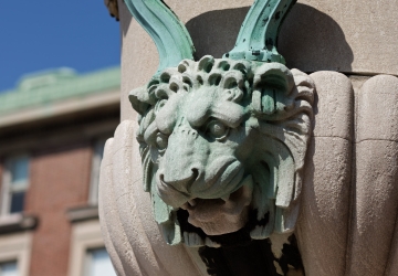 A decorative copper lion's head on a cement urn on campus