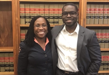 A woman and man both in dark suits, in front of law books 