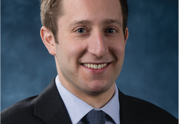 Head shot of man in dark jacket and blue tie. 