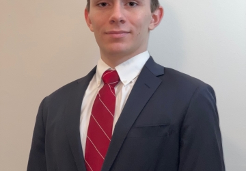 Student in gray suit and red tie stands in front of a white wall