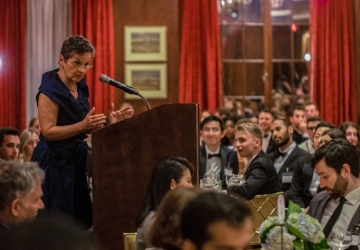 Woman in black dress at podium surrounded by students