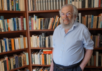 Man with  beard and shirtsleeves in front of bookcases
