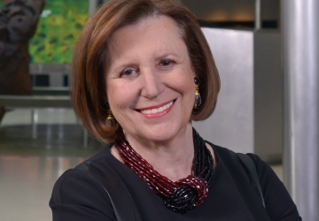 Woman in blue dress and red necklace crossing her arms