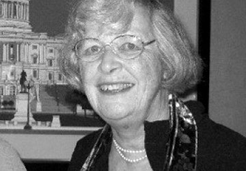 Woman with glasses and gray hair, wearing black jacket and pearls