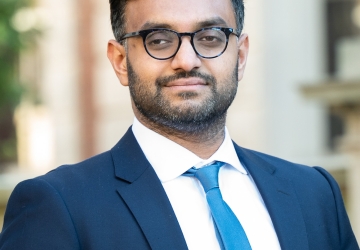 Professor Ashraf Ahmed smiling. He wears glasses with a blue suit and necktie.