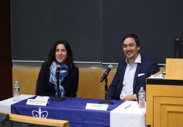 Woman and man sitting at panel table, smiling. 