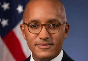Headshot of a man wearing glasses, white shirt, blue tie, and black blazer