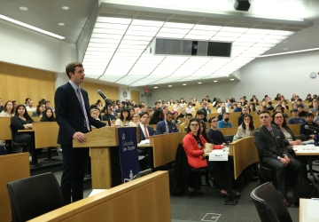 Man standing at a podium in a classroom with audience members seated