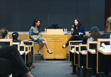 Two women in front of podium speak to an audience