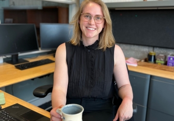 Blonde woman with glasses at desk with coffee mug