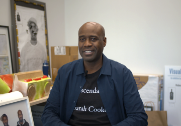 Man wearing a blue collared shirt sitting in front of artwork