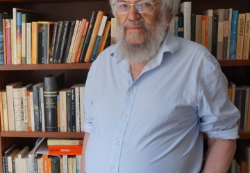 Beareded man in front of wall of bookshelves