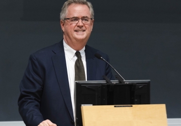 Man in dark suit and glasses at podium