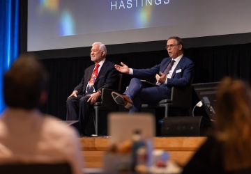 Two men seated onstage for panel discussion, both in suits. 