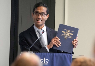 Man in suit and tie holds book at podium