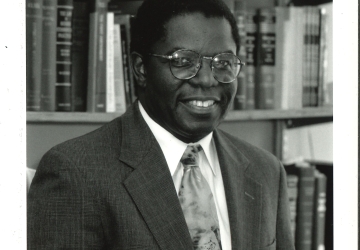 Man in suit and tie holding law book in front of bookshelves