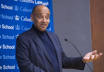 Man speaking at microphone gestures.