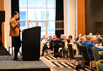 Woman standing at podium speaking to audience seated at tables