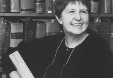 black and white photo of a woman in front of bookcases holding a book 