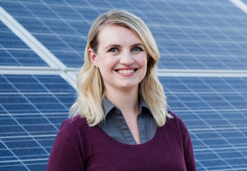 Melanie Scheible ’16 smiles, standing in front of an installation of solar panels.
