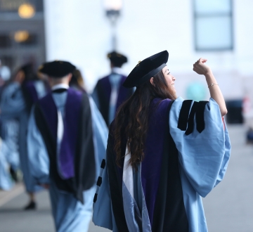 A female graduate waving and wearing regalia at Law School graduation.