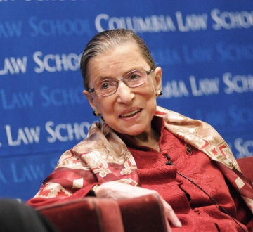 Ruth Bader Ginsburg smiles in front of a blue Columbia Law School backdrop