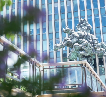 Main Law School building and Bellerophon Taming Pegasus sculpture in background. Trees with leaves and flowers in foreground.