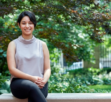 Bhagwati Fellow Sparsha Janardhan sits on a bench outside Jerome Greene Hall