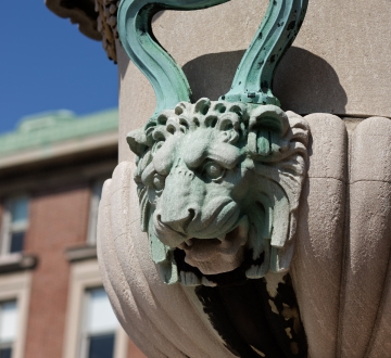 A decorative copper lion's head on a cement urn on campus