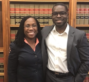 A woman and man both in dark suits, in front of law books 