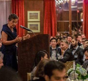 Woman in black dress at podium surrounded by students