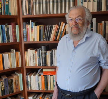 Man with  beard and shirtsleeves in front of bookcases