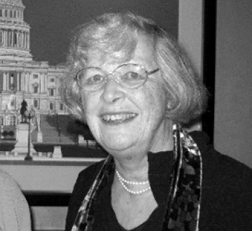 Woman with glasses and gray hair, wearing black jacket and pearls