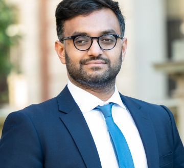 Professor Ashraf Ahmed smiling. He wears glasses with a blue suit and necktie.