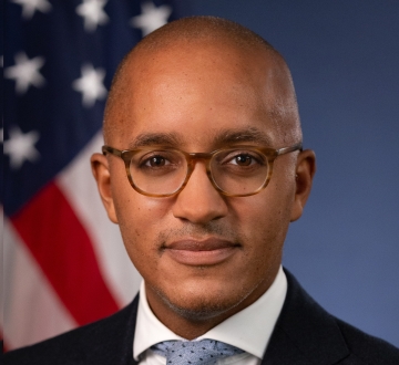 Headshot of a man wearing glasses, white shirt, blue tie, and black blazer