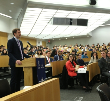 Man standing at a podium in a classroom with audience members seated