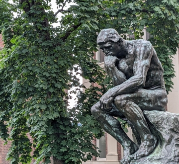 The statue Thinker in front of a green tree in summer