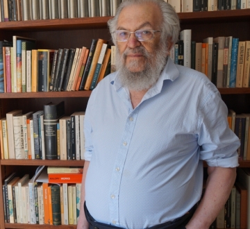 Beareded man in front of wall of bookshelves