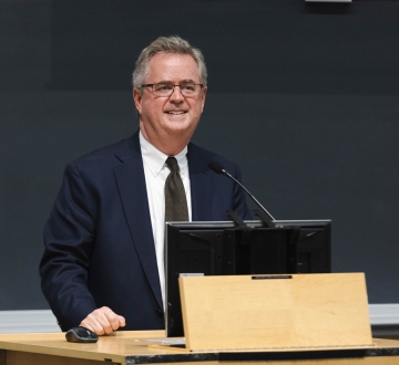 Man in dark suit and glasses at podium