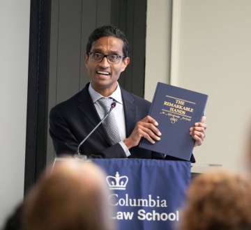 Man in suit and tie holds book at podium