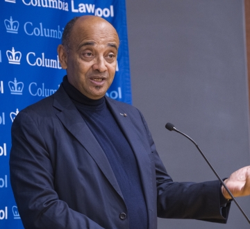 Man speaking at microphone gestures.