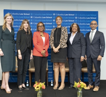 Lineup of five women and a man in professional attire, on a dais.