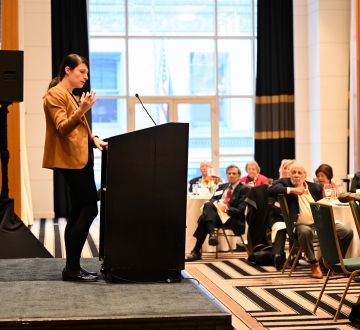 Woman standing at podium speaking to audience seated at tables