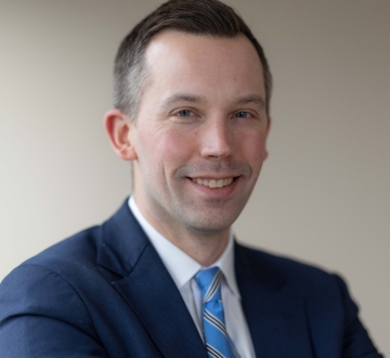 Man with short hair in dark jacket and blue tie