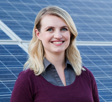 Melanie Scheible ’16 smiles, standing in front of an installation of solar panels.