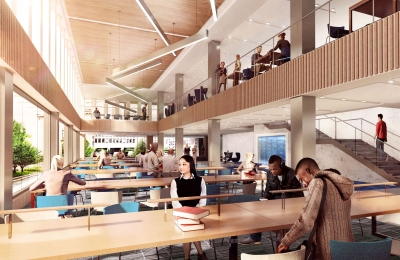 Students sit at long tables next to a bank of windows and beneath a mezzanine.