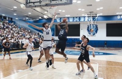 A Columbia Law student jumps up to a basketball hoop while an NYU Law Student jumps to block.